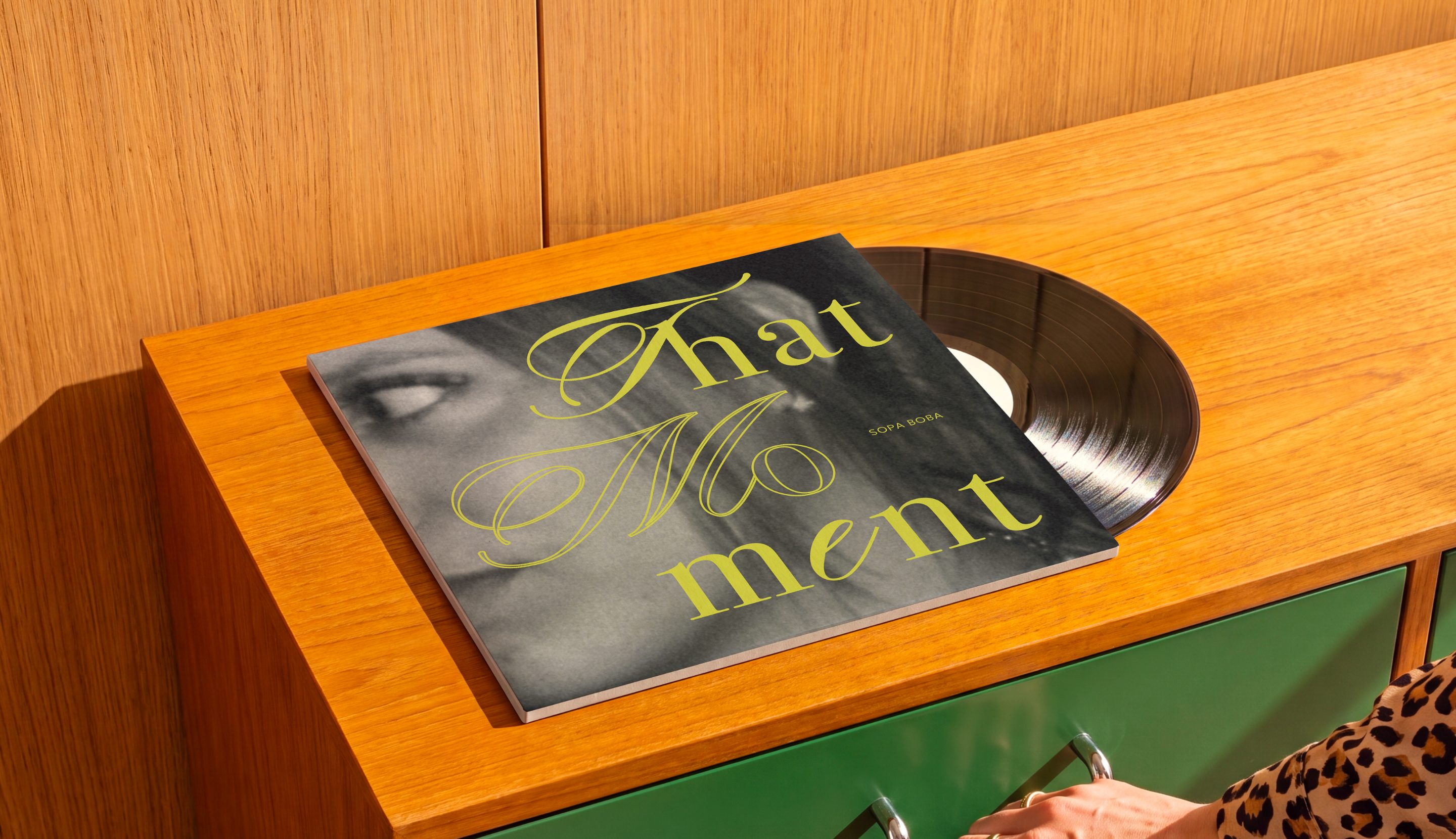 La pochette du vinyle That Moment posée sur une commode en bois aux tiroirs verts, le disque à moitié sorti