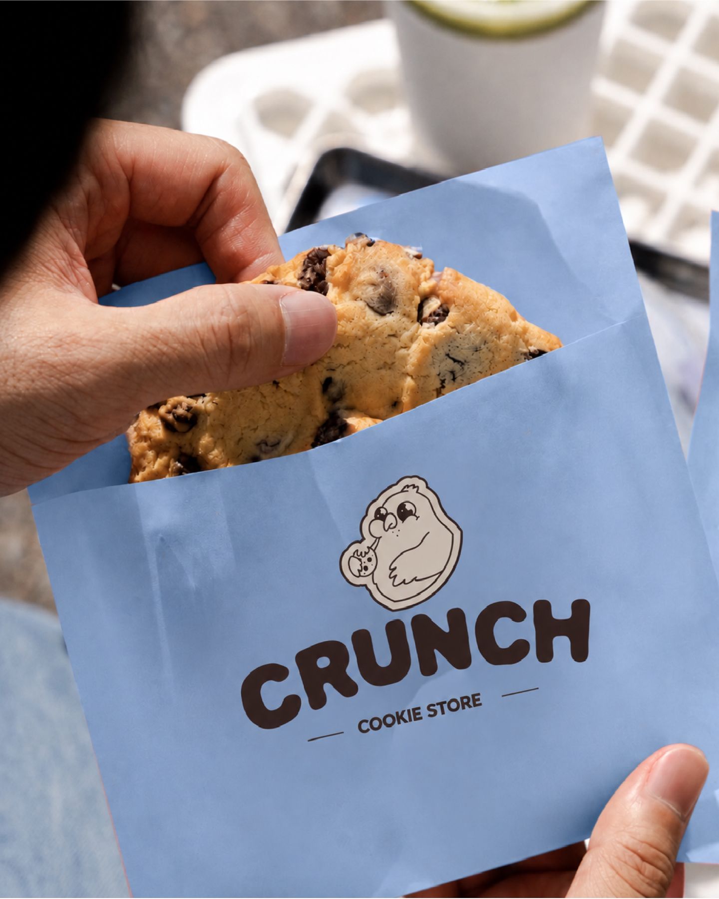 Un cookie qui sort d'un sachet en papier bleu, au logo CRUNCH « cookie store »