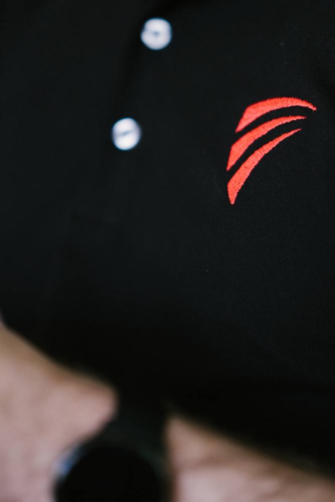 Le détail d'un polo noir : la virgule rouge du logo sur le col