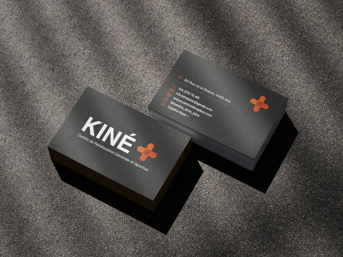 Les cartes de visite KINÉ+ : encre sombre, croix orange, posées sur un fond texturé sable