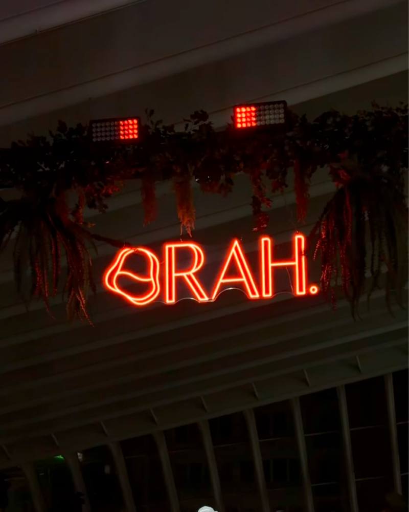 L'enseigne ORAH. en néon orange, suspendue sous un rideau de plantes
