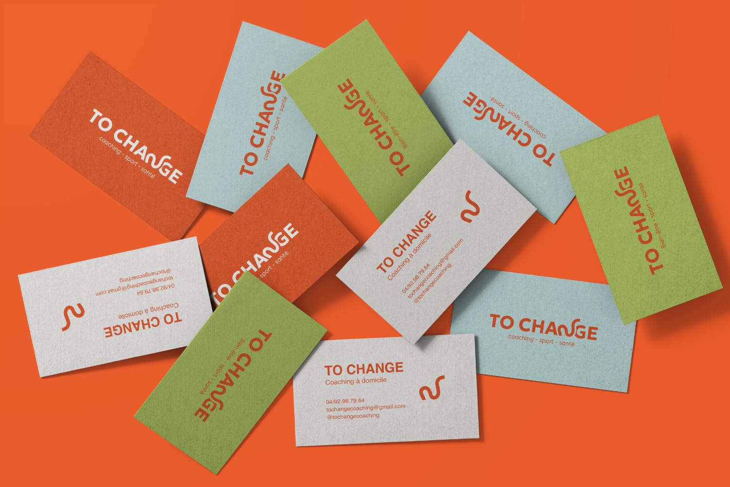 Les cartes de visite To Change éparpillées : orange vif, vert tilleul et blanc, recto au logotype et verso aux coordonnées