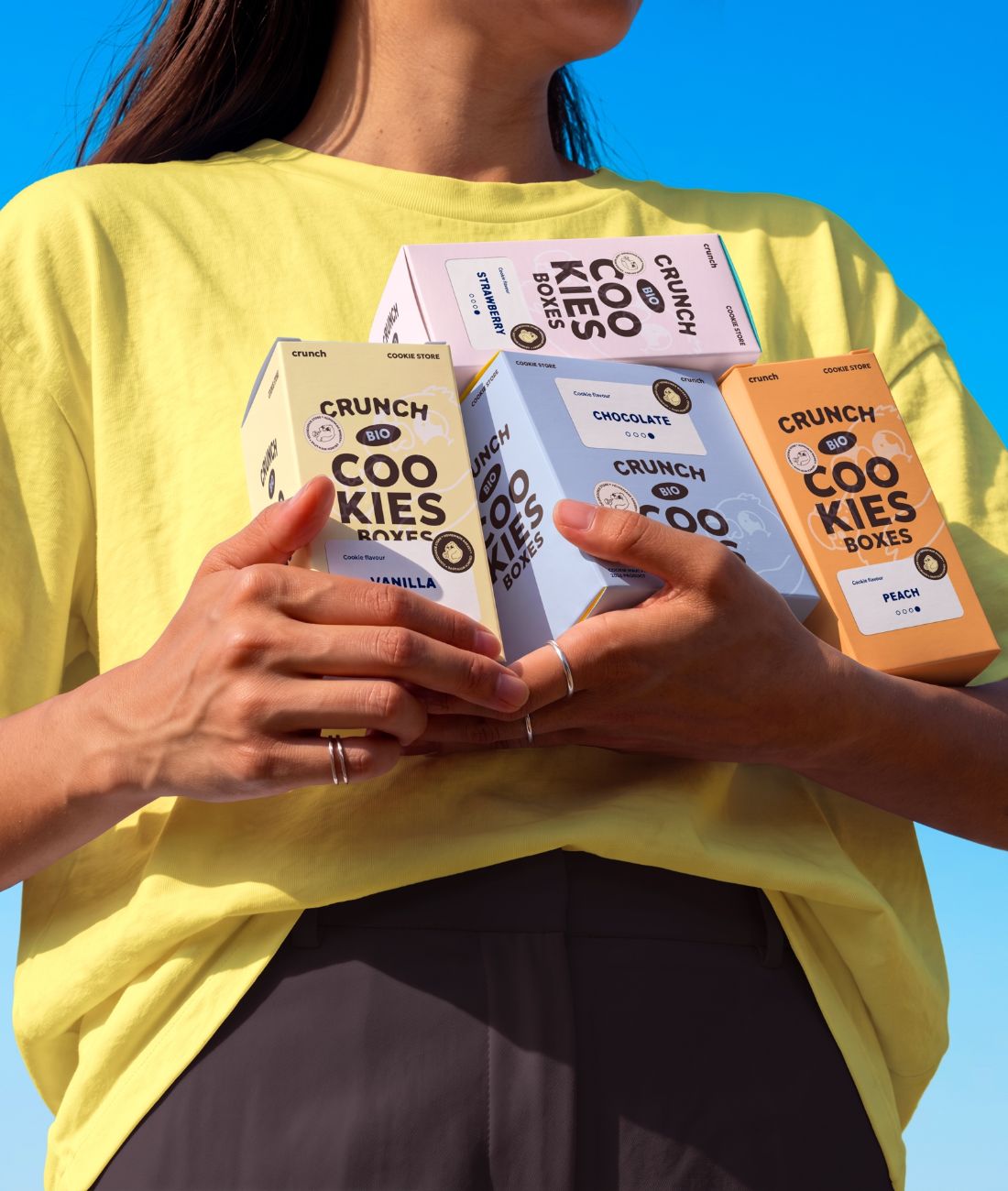 Trois boîtes de cookies CRUNCH serrées contre un t-shirt jaune
